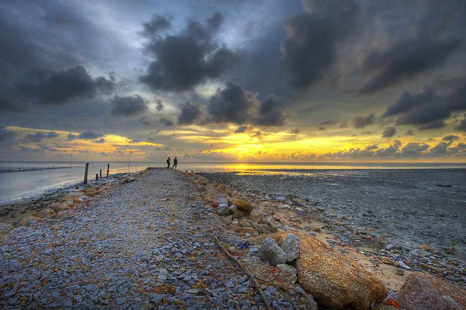 Dua pengunjung berjalan di laluan pesisir menuju matahari terbenam Balik Pulau